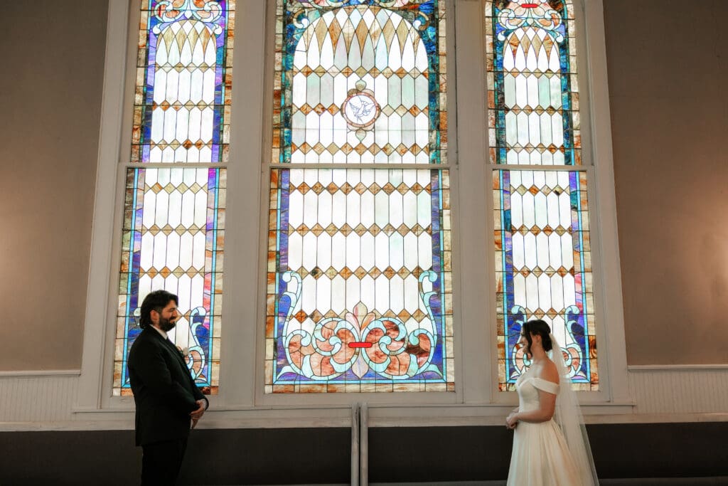 Bride and groom cuddling near the stained glass windows at The 1906 Venue in Whitesboro