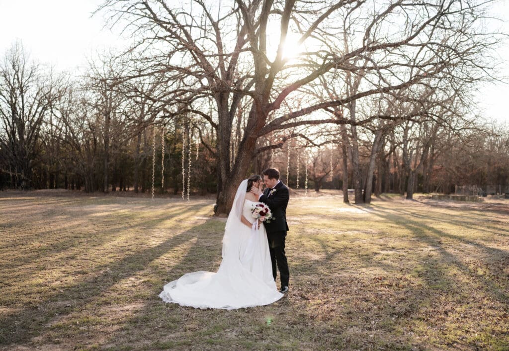Bride and groom embrace in front of a large tree at Soli Deo Gloria Weddings and Events in Decatur, TX