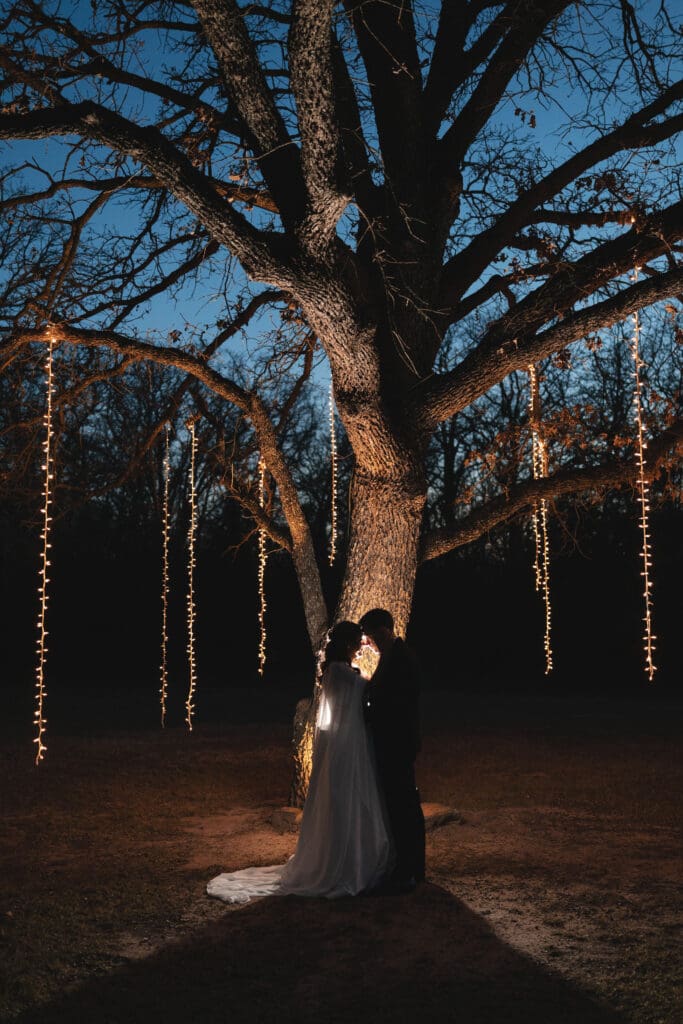 Bride and groom embrace in front of a large tree at Soli Deo Gloria Weddings and Events in Decatur, TX