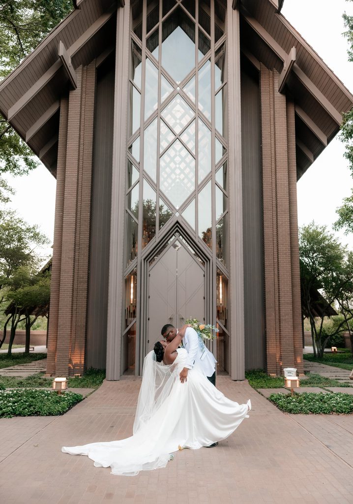 Bride and groom kissing in front of the Marty Leonard Chapel in Fort Worth, TX, one of the best wedding venues in Dallas Fort Worth