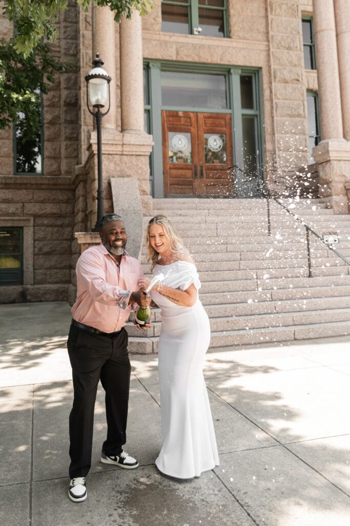 Bride and groom celebrating their intimate Fort Worth courthouse wedding by popping champagne outdoors.