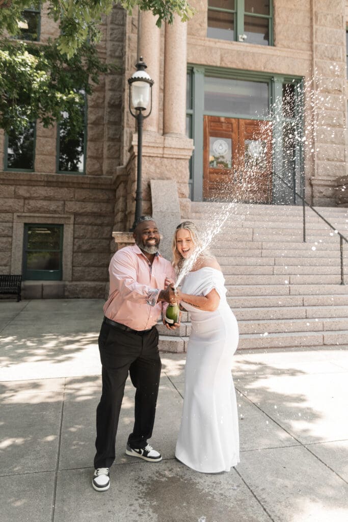 Bride and groom celebrating their intimate Fort Worth courthouse wedding by popping champagne outdoors.