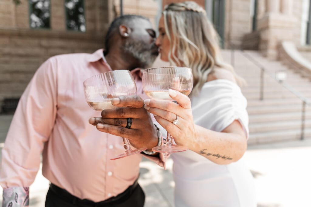 Fort Worth courthouse elopement couple toasting champagne and sharing a kiss outdoors on the courthouse steps.