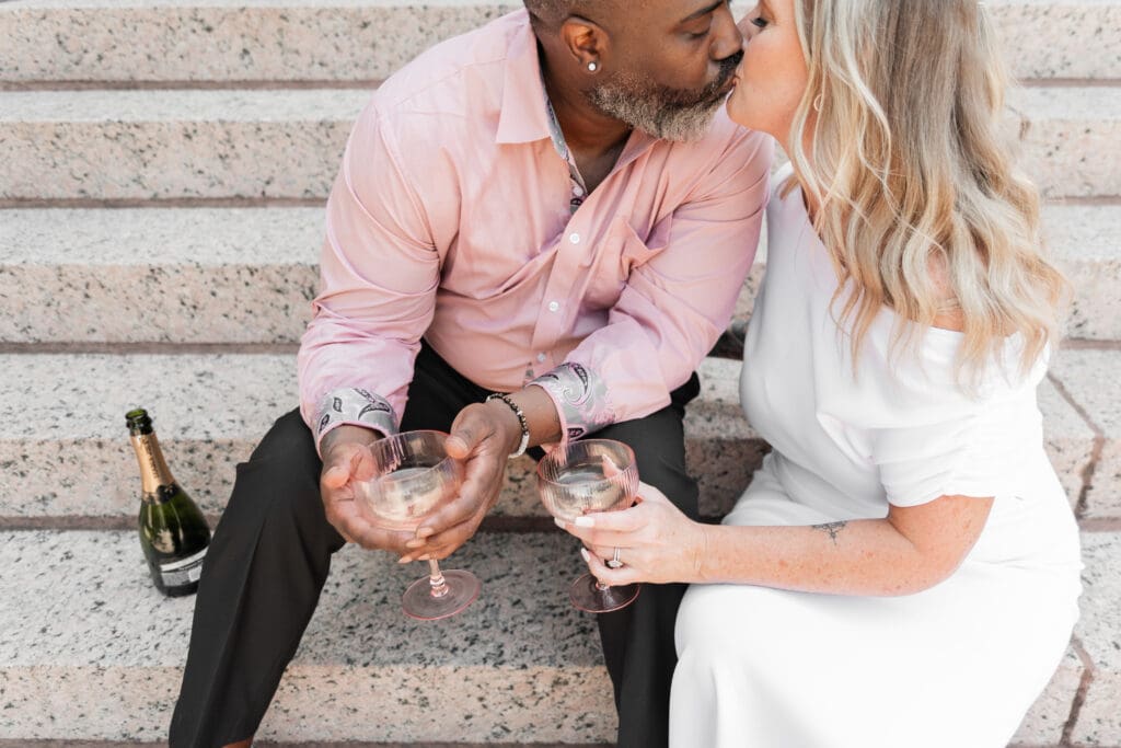 Fort Worth courthouse elopement couple toasting champagne and sharing a kiss outdoors on the courthouse steps.