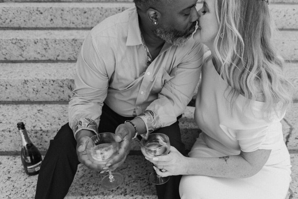 Fort Worth courthouse elopement couple toasting champagne and sharing a kiss outdoors on the courthouse steps.