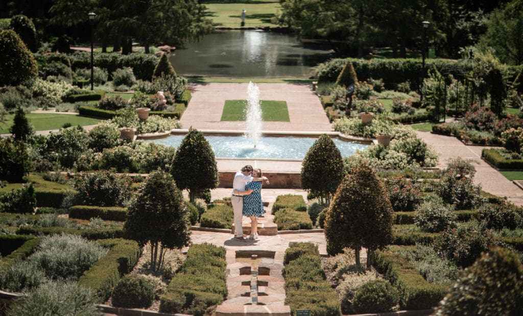 Engaged couple embracing near a fountain at the Fort Worth Botanic Gardens