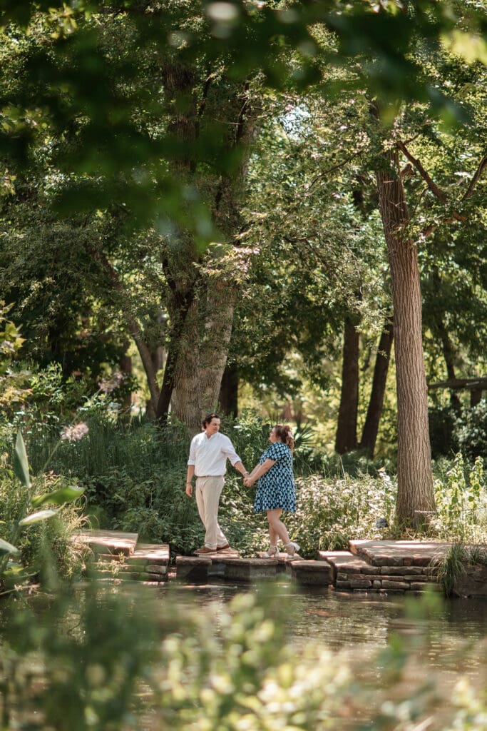 Engaged couple holding hands and walking across water at the Fort Worth Botanic Gardens