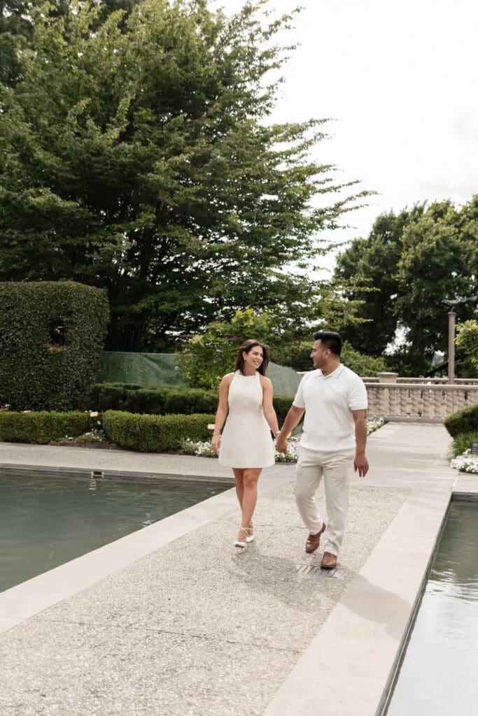 Engaged couple holding hands and walking across water at the Dallas Arboretum