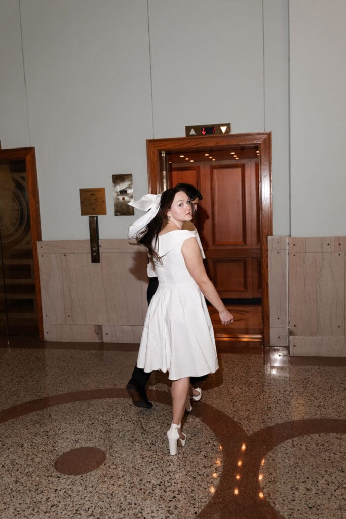 Bride looking back as she walks through the Tarrant County Courthouse towards the elevator during their engagement photos.