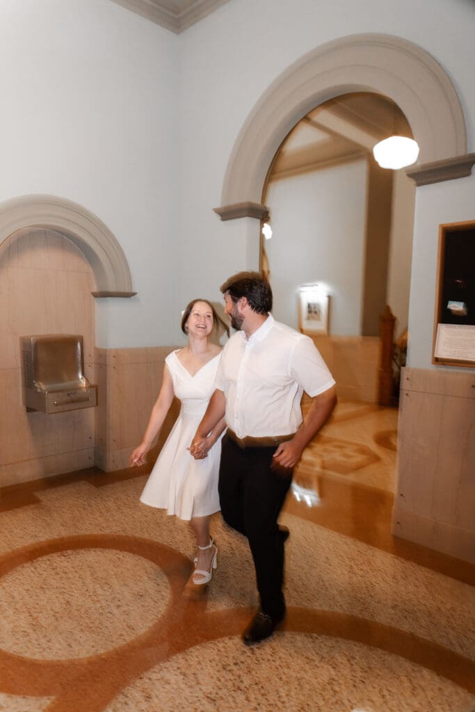Couple walking hand-in-hand inside the Tarrant County Courthouse, smiling and enjoying their engagement session.