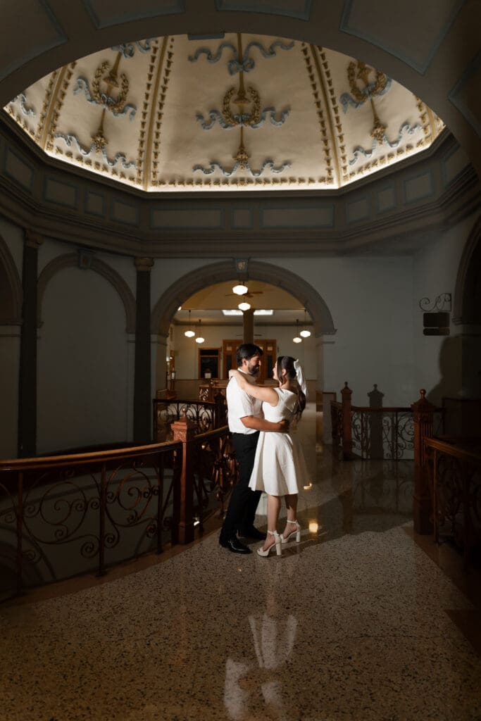 Couple standing on the courthouse balcony, embracing under the historic architecture during their Fort Worth engagement session.