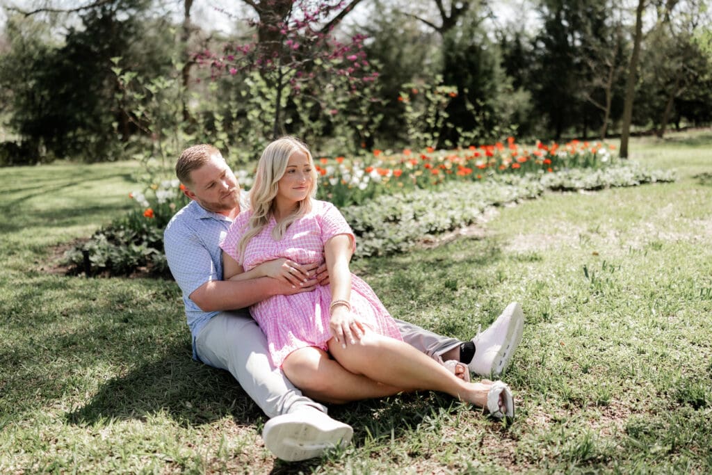 Woman and man cuddling on the lawn at the Fort Worth Botanic Gardens during their engagement session