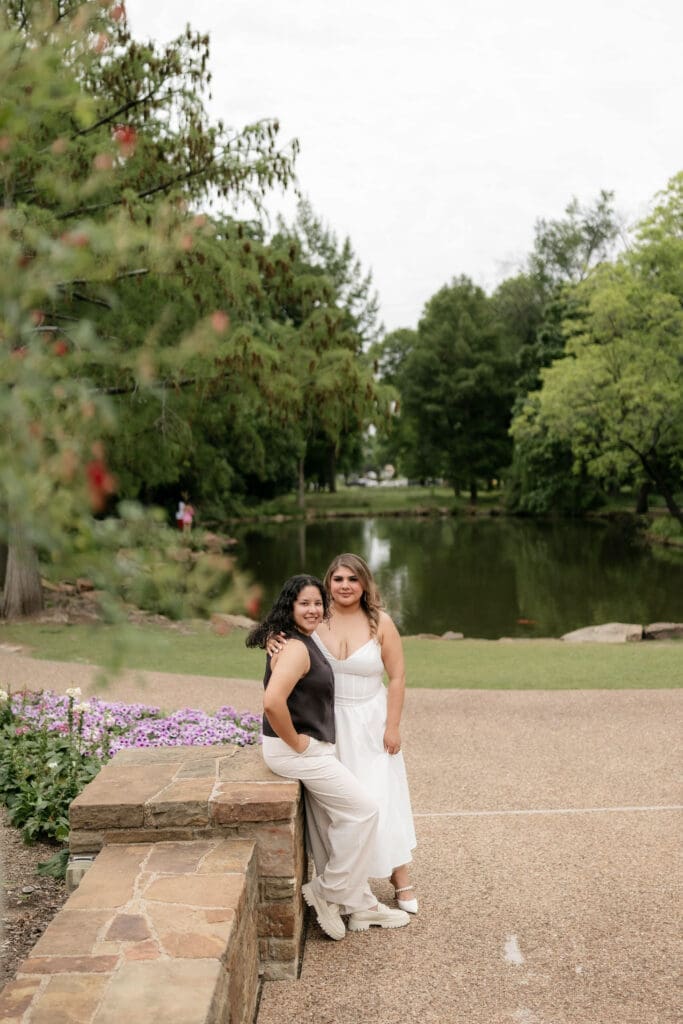 Two brides posing in front of the pond at the Fort Worth Botanic Garden during their engagement session
