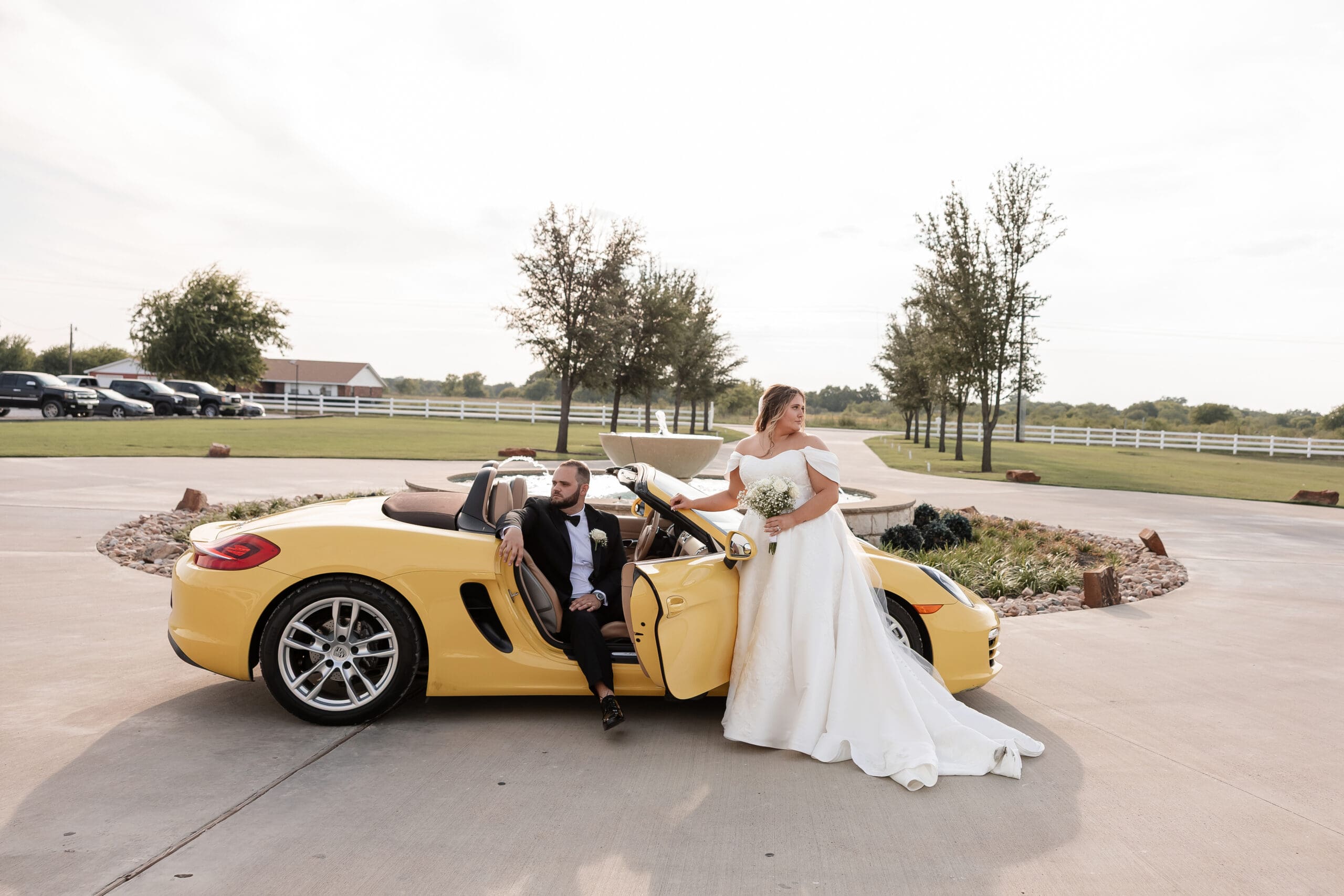Bride and Groom posing with yellow Porsche sports car in front of The Gardenia Venue in Valley View, TX