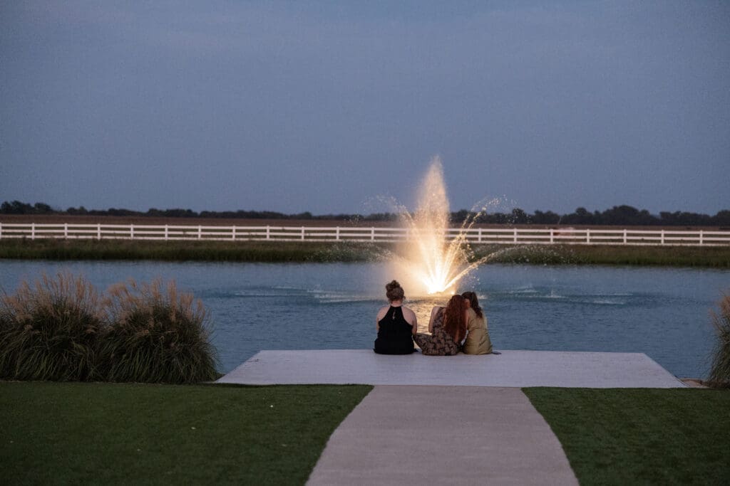 Cousins sitting along the pond at night looking at the water fountain at The Gardenia Venue in Valley View, TX