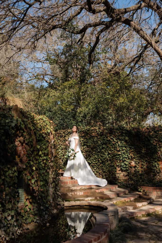 Moody, cinematic bridal portrait of a bride walking along the paths of Chandor Gardens in Weatherford, TX