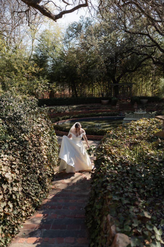 Moody, cinematic bridal portrait of a bride walking along the paths of Chandor Gardens in Weatherford, TX
