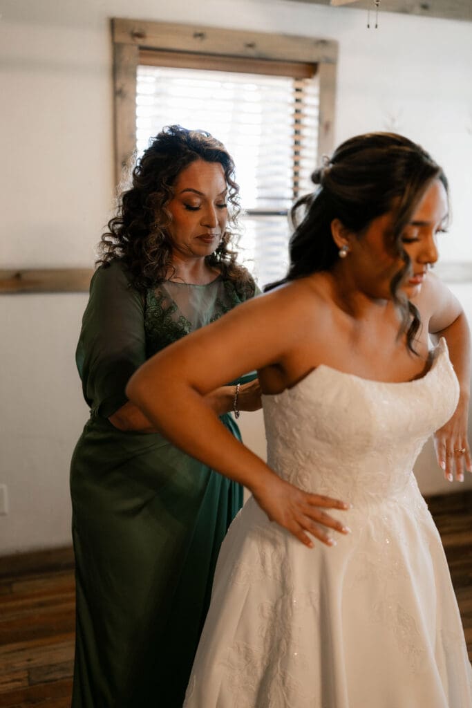 Mother of the bride helping the bride put on her wedding dress