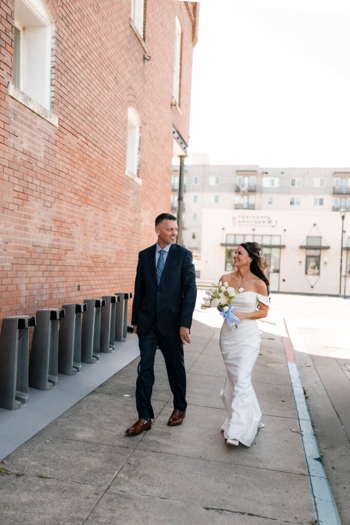 Bride and groom walking down sidewalk outside of Soma Winery in Fort Worth, TX