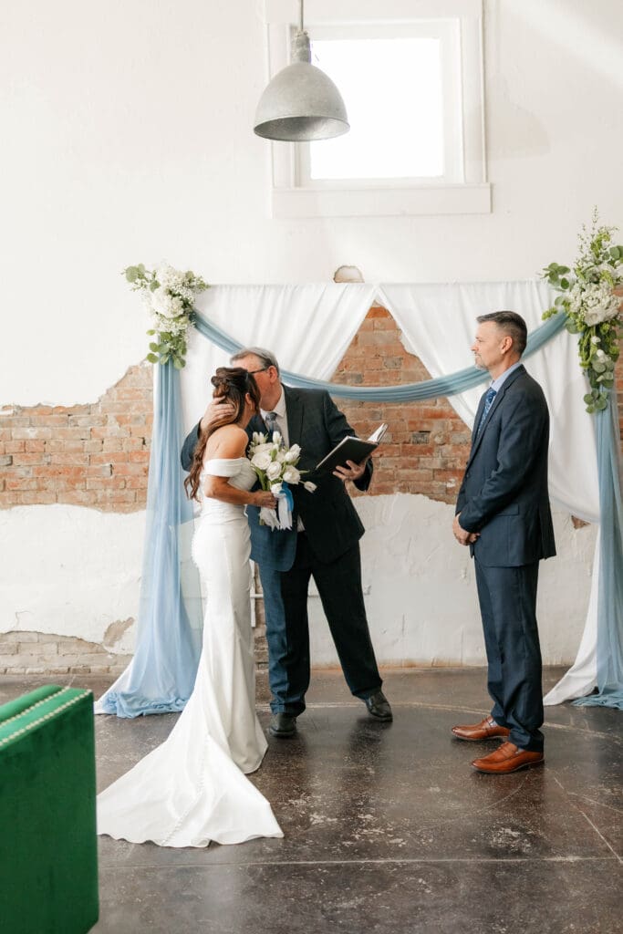 Father of the bride kissing bride before he officiates her wedding at Soma Winery in Fort Worth, TX