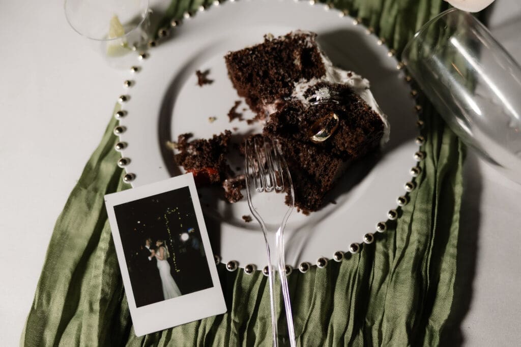 Close up detail shot of bride and groom's rings stuck in their cake alongside party details from the wedding and an instax polaroid of their first dance