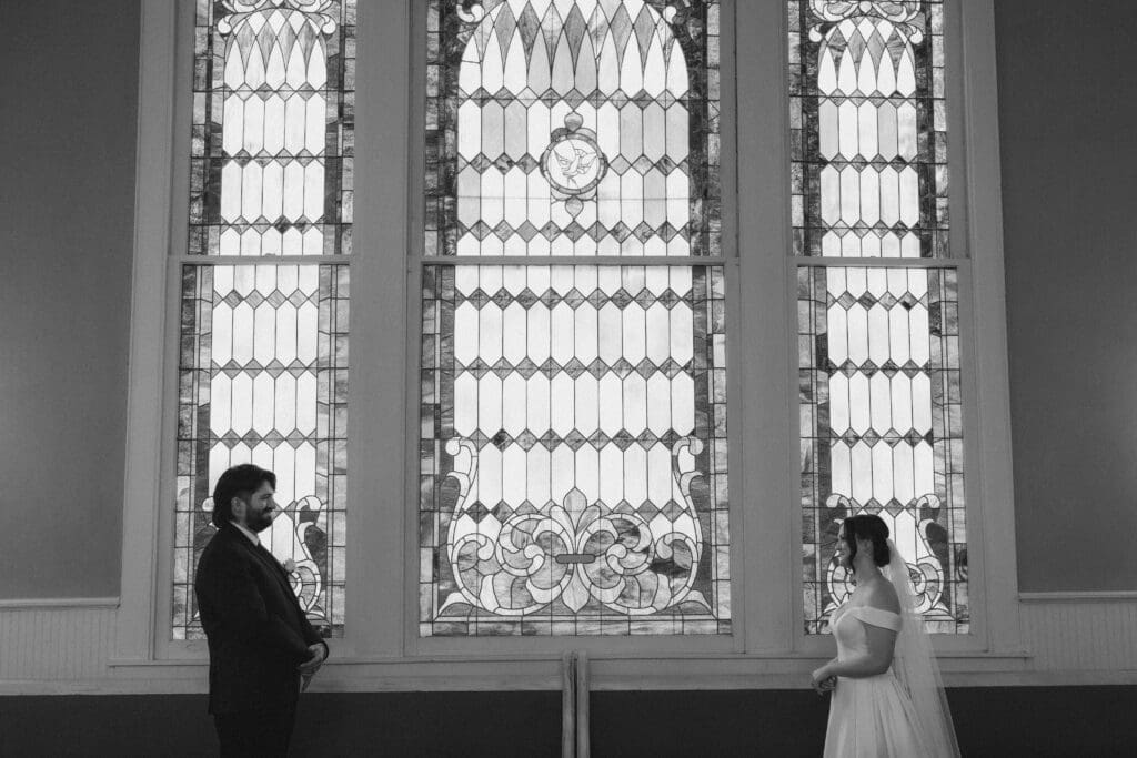 Bride and groom standing in front of large stained glass window at The 1906 venue