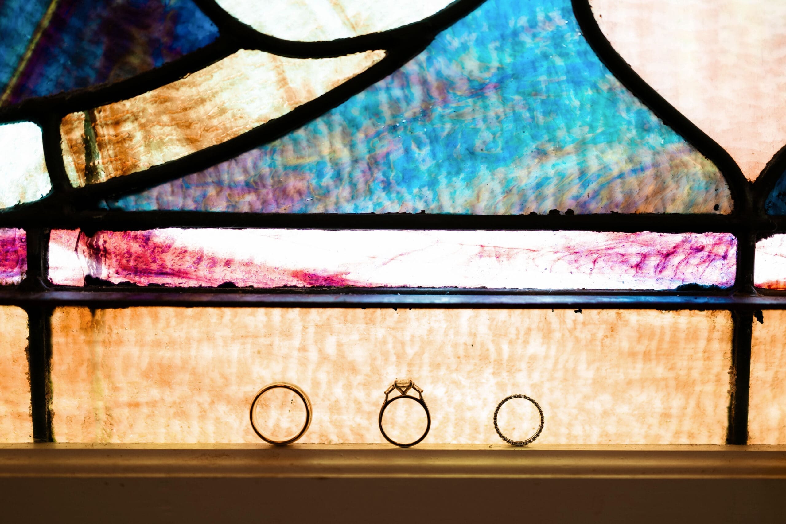 Close-up photo of the bride's and groom's rings in front of stained glass window at The 1906 wedding venue