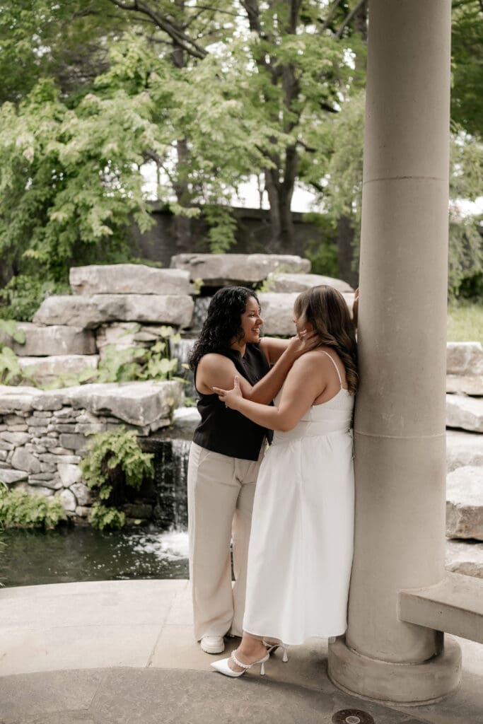 Two women embracing and kissing under a gazebo during their Fort Worth engagement session at the Fort Worth Botanic Garden