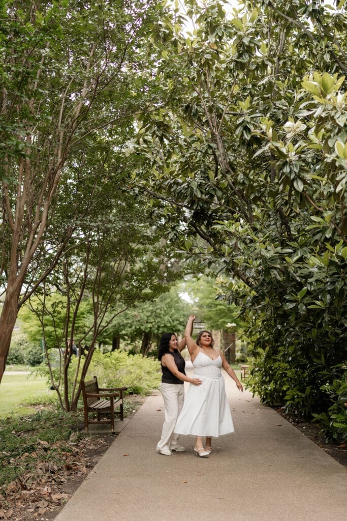 Two women dancing under the magnolia trees during their Fort Worth engagement session at the Fort Worth Botanic Garden