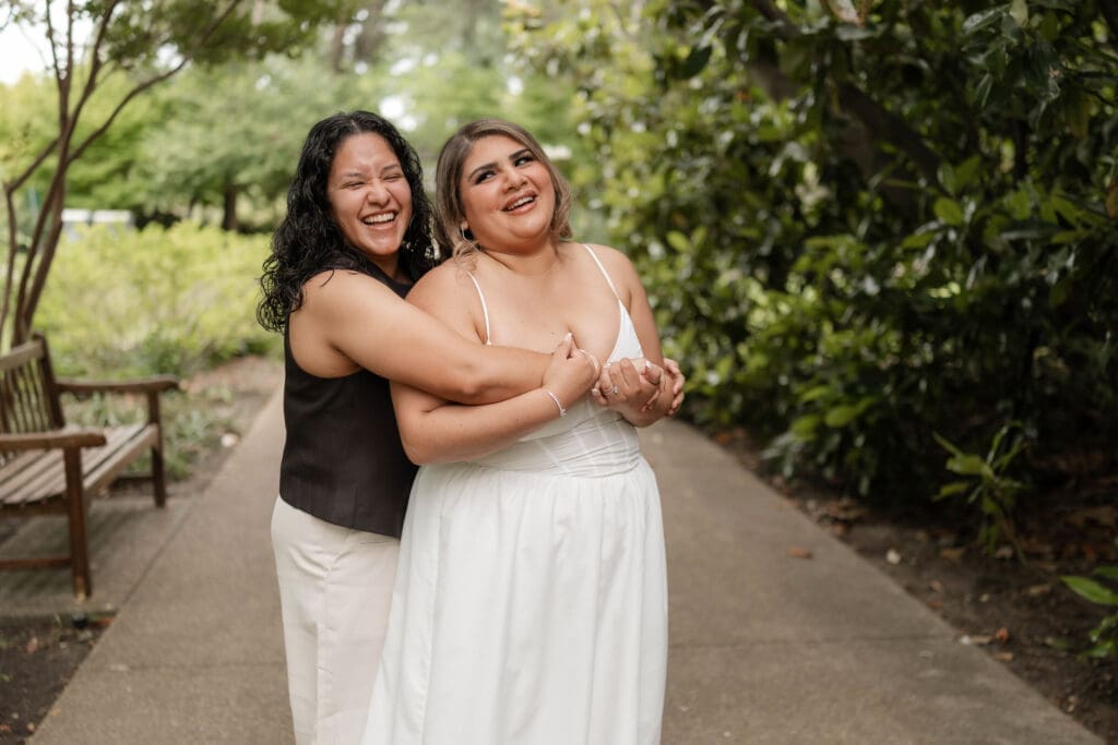 Two women embracing and laughing during their Fort Worth engagement session at the Fort Worth Botanic Garden