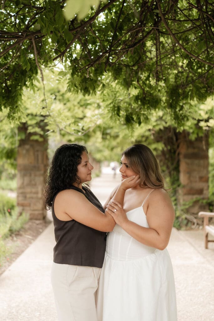 Two women embracing under the wisteria tunnel during their Fort Worth engagement session at the Fort Worth Botanic Garden