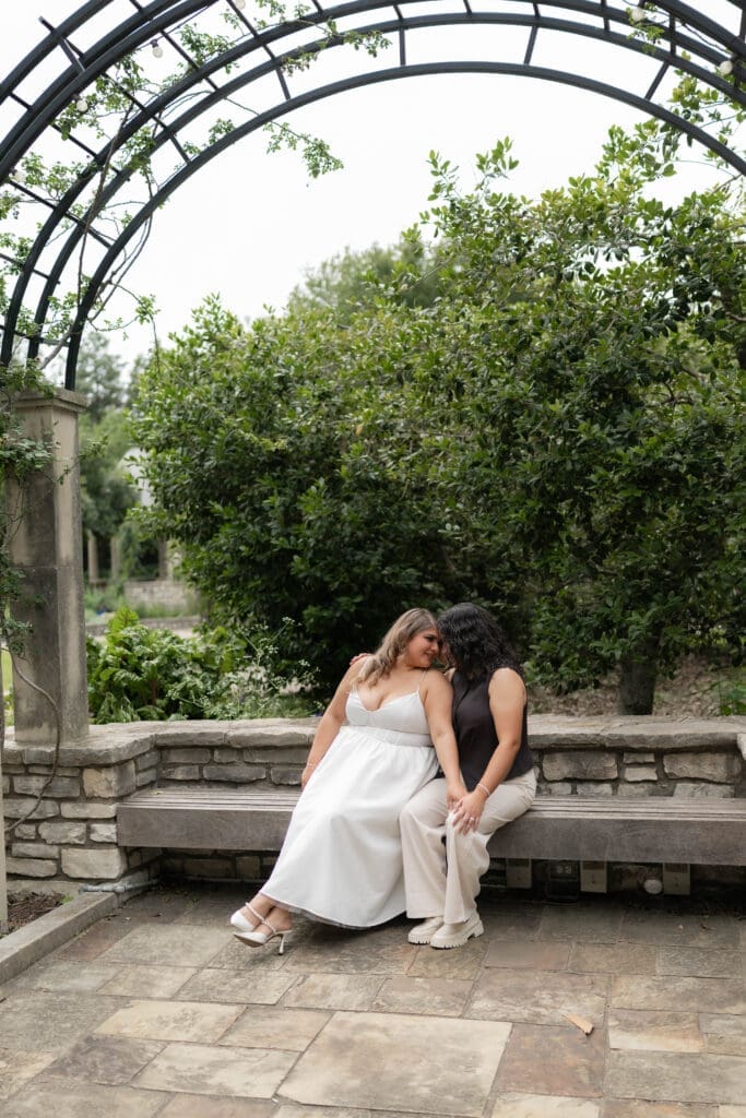Two women snuggling on a bench during their Fort Worth engagement session at the Fort Worth Botanic Garden