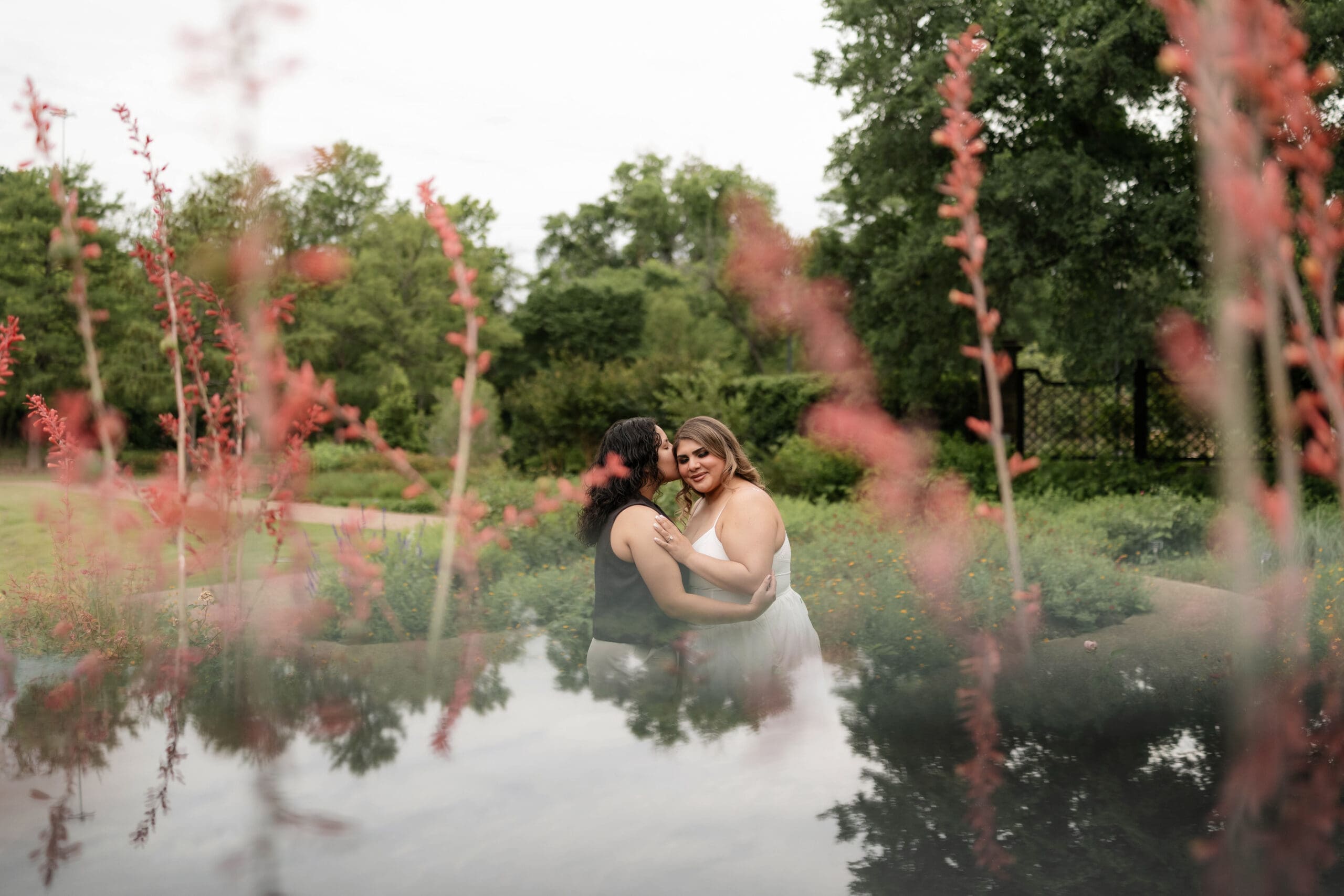 Two women embracing each other in the garden during their Fort Worth engagement session at the Fort Worth Botanic Garden