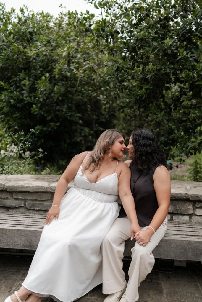 Two women snuggling on a bench during their Fort Worth engagement session at the Fort Worth Botanic Garden