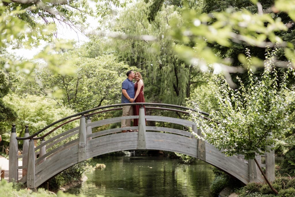 Man and woman embracing on the arched bridge in the Japanese Gardens during their engagement photos at the Fort Worth Botanic Garden in Fort Worth, TX