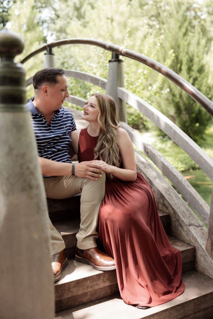 Man and woman embracing on the arched bridge in the Japanese Gardens during their engagement photos at the Fort Worth Botanic Garden in Fort Worth, TX