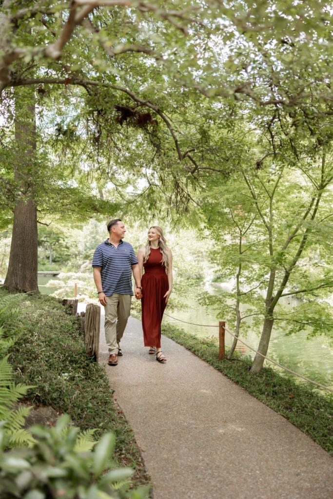 Man and woman walking, holding hands in the Japanese Gardens during their engagement photos at the Fort Worth Botanic Garden in Fort Worth, TX
