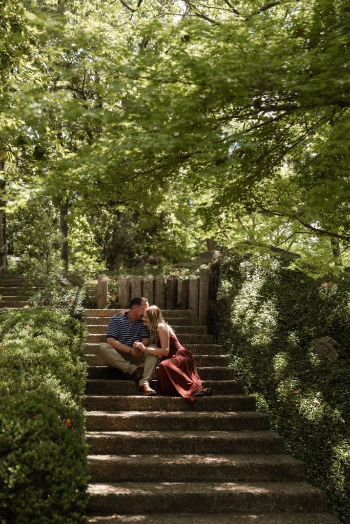 Man and woman cuddling on the steps in the Japanese Garden in the Fort Worth Botanic Garden during their proposal engagement session in Fort Worth, TX