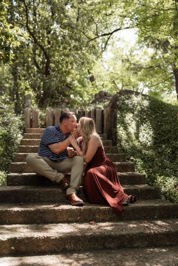 Man and woman cuddling on the steps in the Japanese Garden in the Fort Worth Botanic Garden during their proposal engagement session in Fort Worth, TX