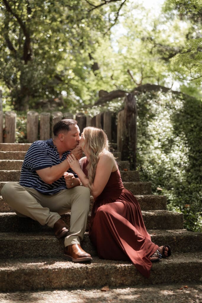 Man and woman cuddling on the steps in the Japanese Garden in the Fort Worth Botanic Garden during their proposal engagement session in Fort Worth, TX