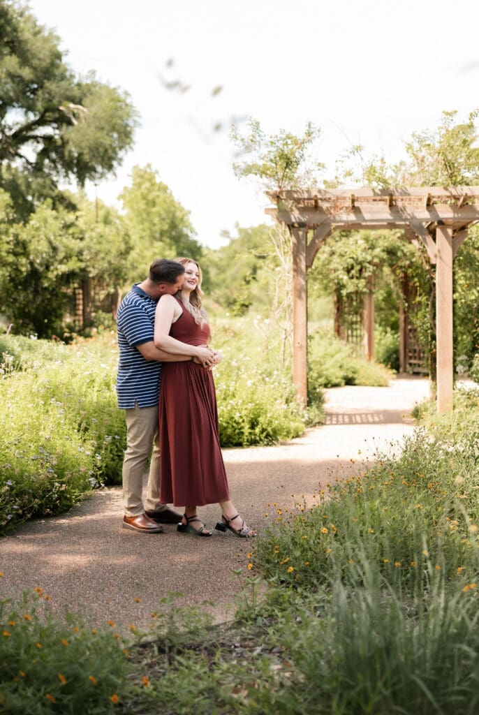Man and woman cuddling in the Fort Worth Botanic Garden during their proposal engagement session in Fort Worth, TX