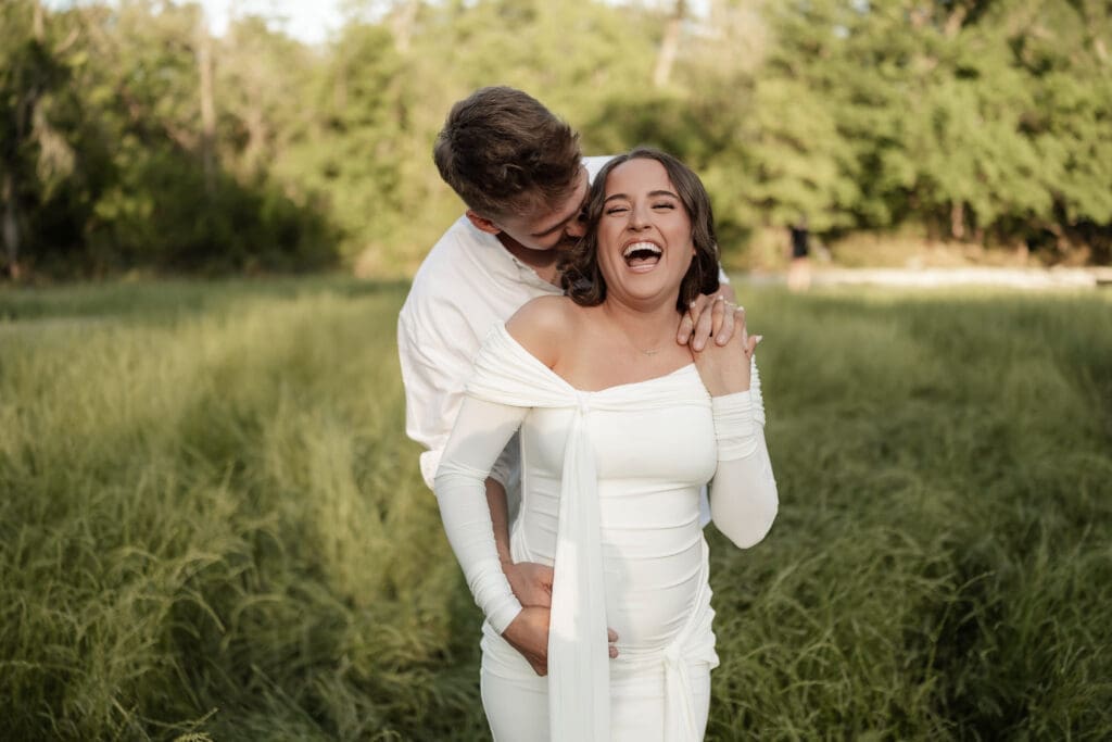 Couple laughing in the grassy field during their golden hour Airfield Falls Maternity session