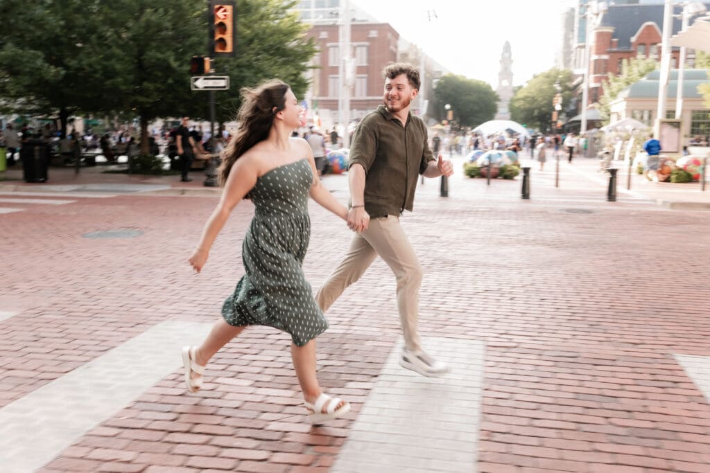 Man and woman running across a crosswalk in Sundance Square, Fort Worth, TX during their engagement photo session
