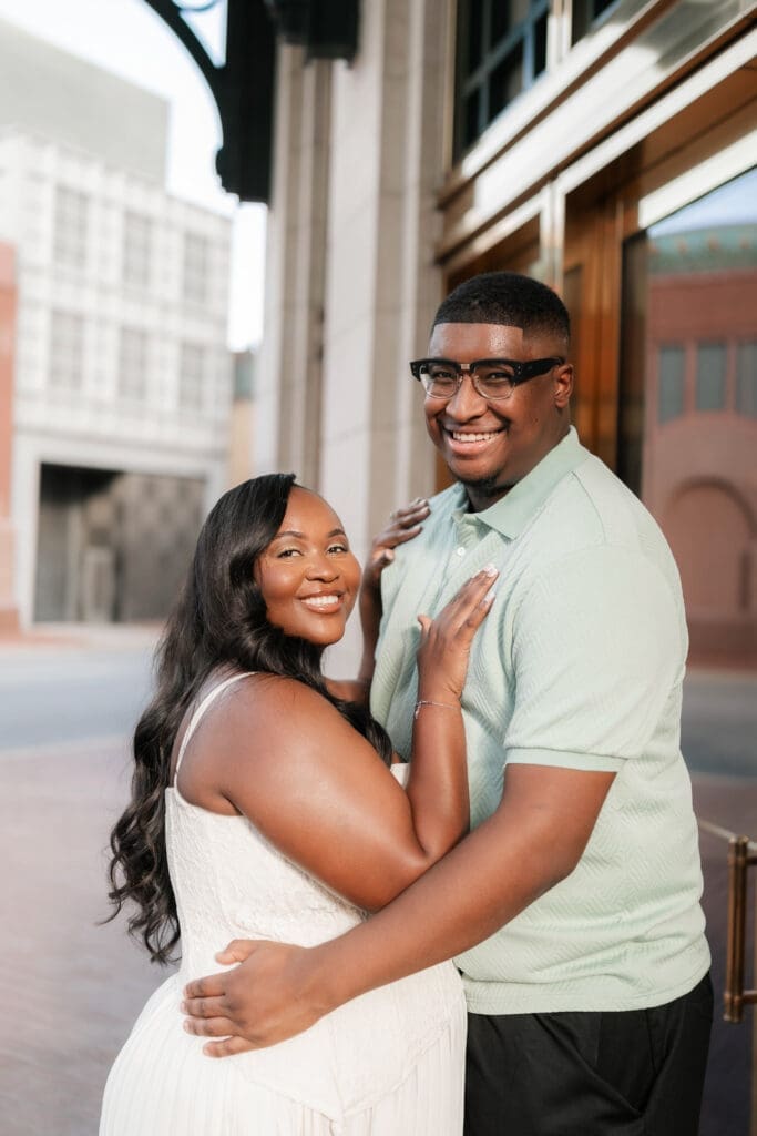 Couple snuggling outside of Bass Hall during their golden hour engagement session in Fort Worth, TX