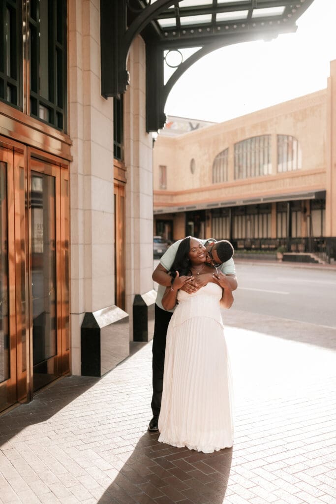 Couple snuggling outside of Bass Hall during their golden hour engagement session in Fort Worth, TX