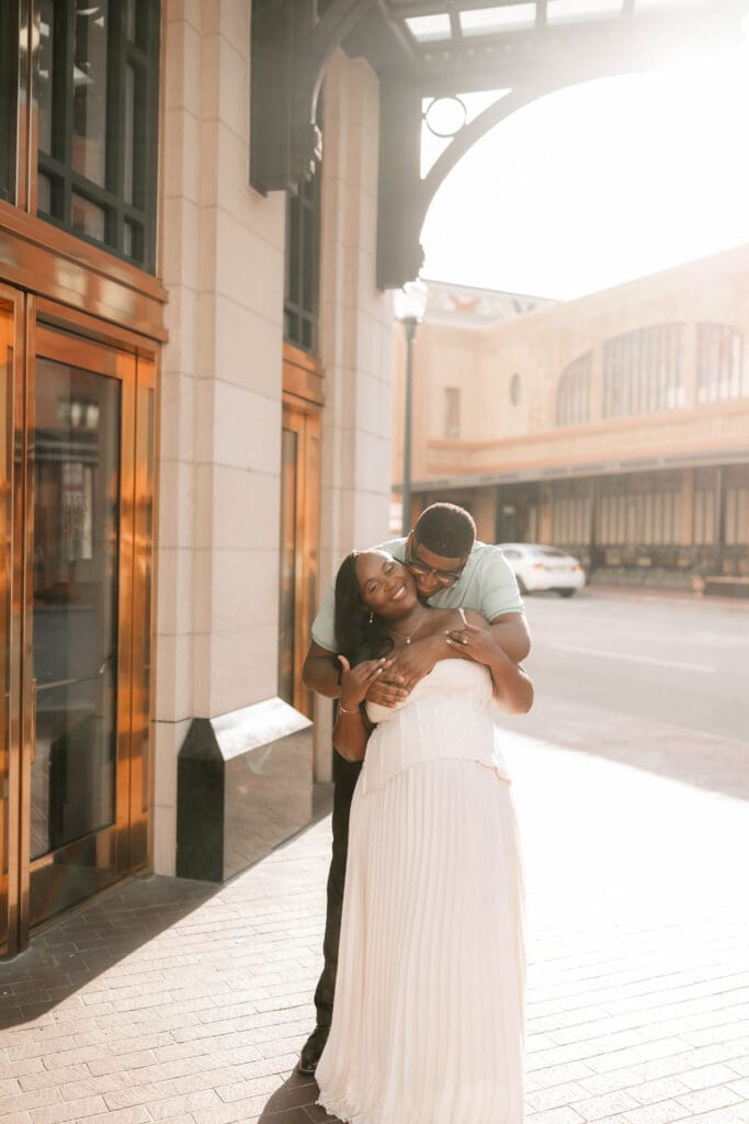 Couple snuggling outside of Bass Hall during their golden hour engagement session in Fort Worth, TX