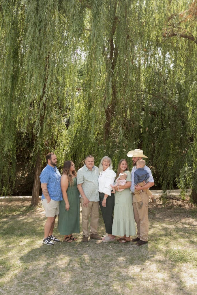 Family laughing while posing in front of the willow tree at Airfield Falls in Fort Worth during their family portraits 