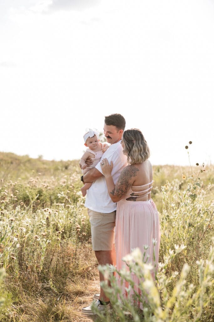 Husband and wife holding their baby standing in the field at Tandy Hills in Fort Worth for their family photography session