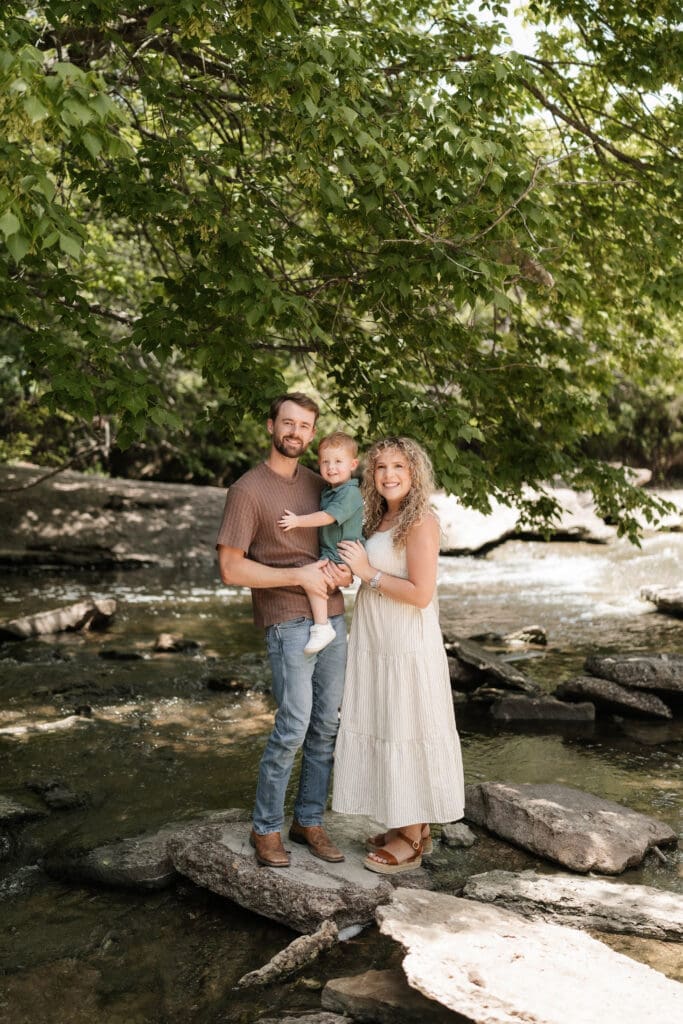 Husband and wife with their toddler standing in the creek at Ikard Trail in Weatherford for family photos