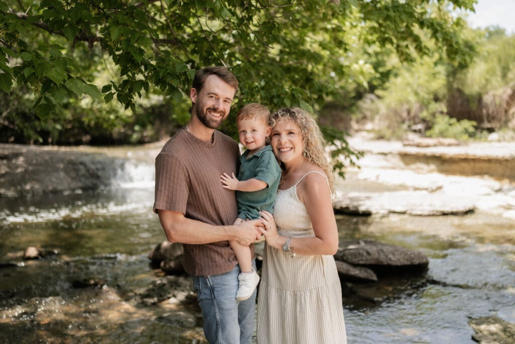 Husband and wife with their toddler standing in the creek at Ikard Trail in Weatherford for family photos